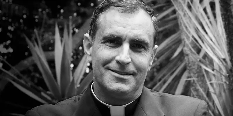 Padre Ignacio María Doñoro en blanco y negro, sacerdote sonriendo levemente, con un alzacuellos blanco, hablando sobre el rescate de niños en el Amazonas peruano.